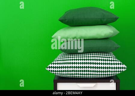 Pile de coussins sur une table de nuit en bois contre un mur intérieur vert Banque D'Images