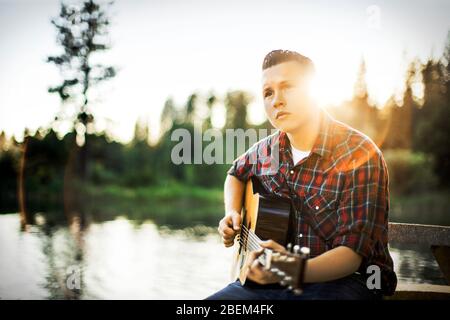 Jeune homme jouant de la guitare près d'un lac Banque D'Images