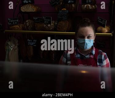 Sylvya, employée de le pain Guina dans le 9ème Arrondissement, pose pendant son déplacement derrière le comptoir gardé par emballage plastique à Paris, France, le 8 avril 2020. « il est important de rester ouvert pour les gens car sinon les gens n'auront rien », a-t-elle dit. Comme élément de base de la culture française, de nombreuses boulangeries sont restées ouvertes à Paris pendant la fermeture du Covid-19. Ainsi, des boulangers et des employés ont été jetés sur les lignes avant de la pandémie, portant souvent des masques de visage et travaillant derrière des comptoirs protégés par un emballage en plastique ou du plexiglass pour continuer à servir les gens et à maintenir un Banque D'Images