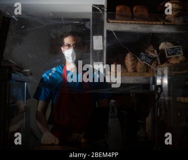 Jules, un employé de Tout Autour du pain dans le 3ème Arrondissement, pose pendant son déplacement derrière le comptoir protégé par un emballage plastique, à Paris, France, le 12 avril 2020. Comme élément de base de la culture française, de nombreuses boulangeries sont restées ouvertes à Paris pendant la fermeture du Covid-19. Ainsi, des boulangers et des employés ont été jetés sur les lignes de front de la pandémie, portant souvent des masques de visage et travaillant derrière des comptoirs protégés par un emballage en plastique ou du plexiglass pour continuer à servir les gens et maintenir un semblant de normalité. (Photo de Daniel Brown/Sipa USA) Banque D'Images