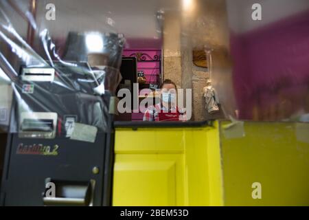 Sylvya, employée de le pain Guina dans le 9ème Arrondissement, pose pendant son déplacement derrière le comptoir gardé par emballage plastique à Paris, France, le 8 avril 2020. « il est important de rester ouvert pour les gens car sinon les gens n'auront rien », a-t-elle dit. Comme élément de base de la culture française, de nombreuses boulangeries sont restées ouvertes à Paris pendant la fermeture du Covid-19. Ainsi, des boulangers et des employés ont été jetés sur les lignes avant de la pandémie, portant souvent des masques de visage et travaillant derrière des comptoirs protégés par un emballage en plastique ou du plexiglass pour continuer à servir les gens et à maintenir un Banque D'Images