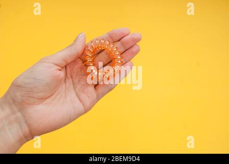 Ressort élastique pour cheveux dans les mains, orange sur fond jaune. Banque D'Images