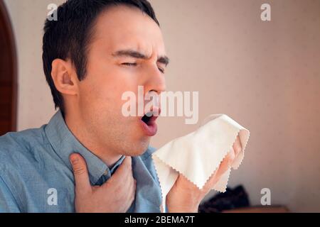 L'homme tousse. Un jeune homme d'affaires tousse dans une serviette de rag pour propager les germes viraux. Toussez dans un chiffon Banque D'Images