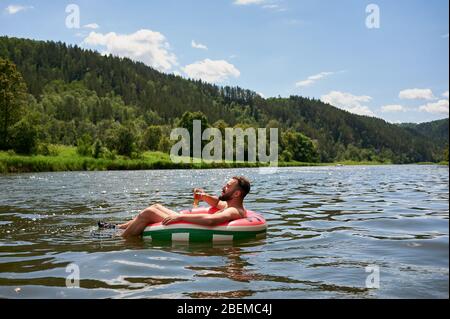 Profiter de la vie. Jeune homme reposant avec un verre de bière sur la rivière. Détente, vacances, concept de style de vie Banque D'Images