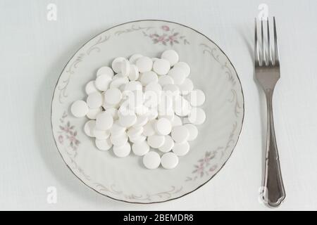 De nombreuses comprimés ronds blancs se trouvent dans une plaque en porcelaine blanche. Traitement au lieu de nourriture. Pilules de vitamine Banque D'Images
