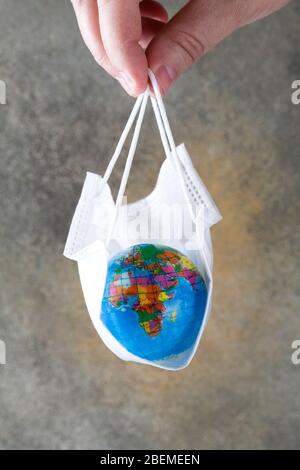 La main humaine maintient la terre posée dans le masque médical sur fond gris. Sauver la planète du virus corona. Réduire le risque d'infection et de propagation du virus. Banque D'Images