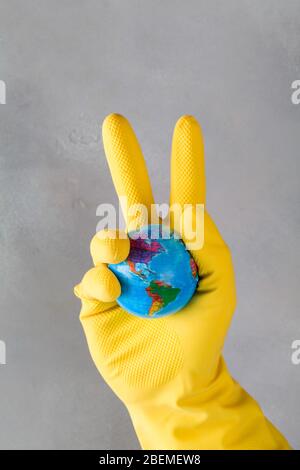 La main humaine dans le gant jaune maintient la terre sur fond bleu. Sauver la planète du virus corona. Réduire le risque d'infection et de propagation du virus. Victoire co Banque D'Images