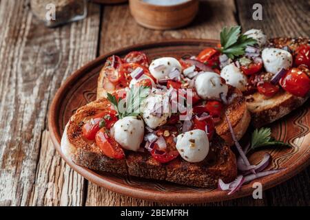 Bruschetta de tomates avec mozzarella et herbes dans un bol en céramique rural, gros plan Banque D'Images