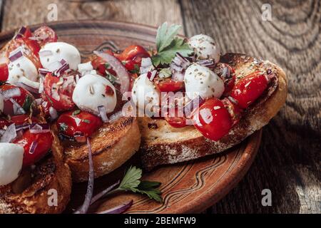 Bruschetta de tomates avec mozzarella et herbes dans un bol en céramique rural, gros plan Banque D'Images