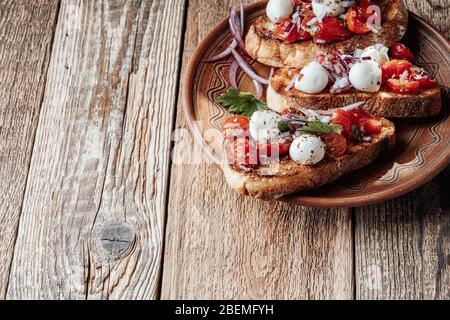 Bruschetta de tomates avec mozzarella et herbes dans un bol en céramique rural, gros plan Banque D'Images