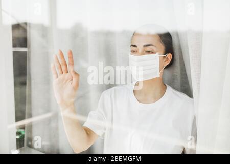 Médecin fatigué dans le masque médical regardant par la fenêtre. Travail important et auto-isolement pendant la pandémie de coronavirus. Espoir pour la médecine. Banque D'Images