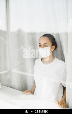 Médecin fatigué dans le masque médical regardant par la fenêtre. Travail important et auto-isolement pendant la pandémie de coronavirus. Espoir pour la médecine. Banque D'Images