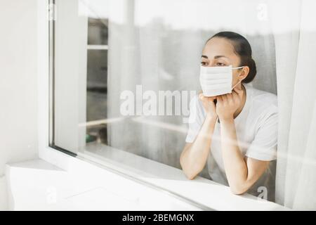 Médecin fatigué dans le masque médical regardant par la fenêtre. Travail important et auto-isolement pendant la pandémie de coronavirus. Espoir pour la médecine. Banque D'Images