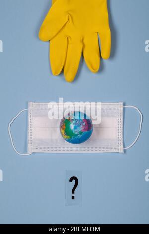 gant jaune, terre posée sur le masque médical et point d'interrogation sur fond bleu. concept ce qui est le prochain. Sauver la planète du virus corona. Réduire le risque de In Banque D'Images