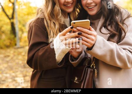 Image recadrée de deux jeunes filles gaies portant des manteaux marchant ensemble dans la forêt d'automne