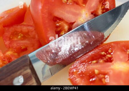 Vue rapprochée d'un couteau à steak avec une poignée en bois qui tranché à travers une tomate rouge à beefsteak sur un tableau de découpe. Banque D'Images