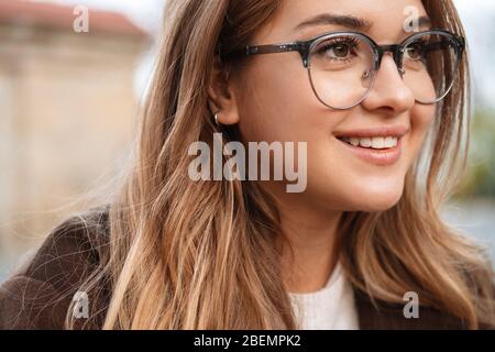 Gros plan sur une jeune fille blonde souriante portant des lunettes donnant sur l'extérieur Banque D'Images