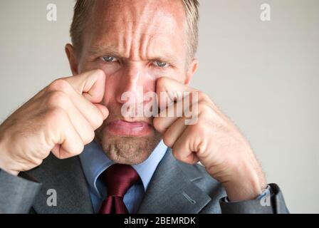 Poupe un homme d'affaires qui prétend essuyer les larmes de ses joues avec une expression triste exagérée Banque D'Images