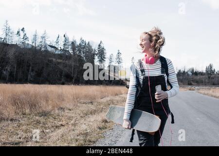 femme marchant avec joie avec son skateboard et son tapis de yoga chant Banque D'Images