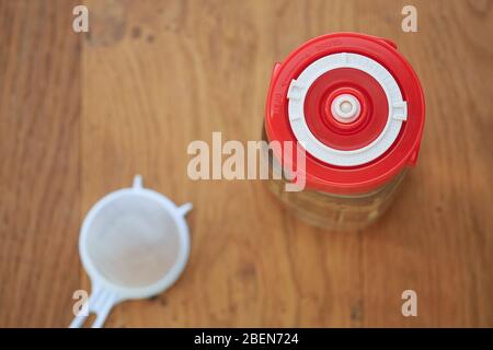 Une prise en charge d'un pot en verre contenant du kéfir d'eau et scellé avec un couvercle de fermentation rouge vif indiquant la date actuelle. Concept de santé l Banque D'Images