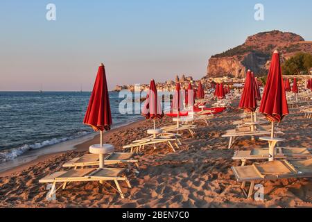 Dans l'atmosphère de crépuscule, des parasols fermés devant la ville de Cefalù avec son célèbre rocher Banque D'Images