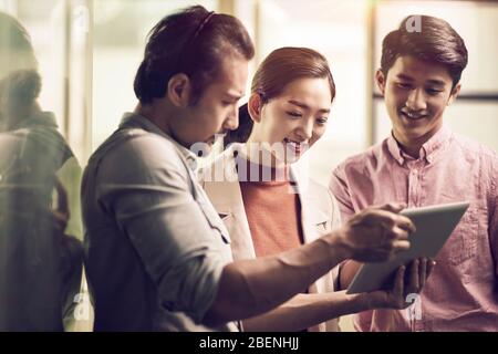 trois jeunes entrepreneurs asiatiques travaillant ensemble au bureau à la recherche d'une tablette numérique Banque D'Images