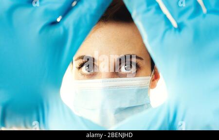 Femme portant un masque médical bleu et des gants en latex tenant sa main devant son visage Banque D'Images