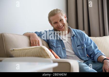 Jeune homme souriant se reposant sur un canapé à la maison regarder l'appareil photo, portrait. Banque D'Images