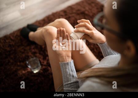Jeune femme blanche à la maison Holding deux pilules de douleur Killer dans sa main Palm après avoir renversé de bouteille et de verre d'eau. Banque D'Images