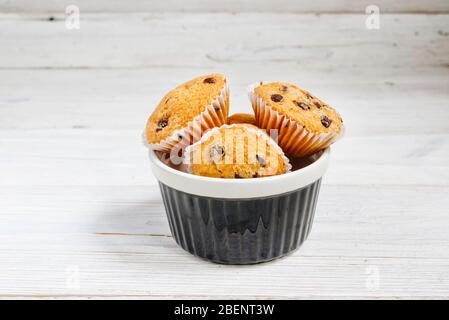 Petits muffins avec des copeaux de chocolat dans un bol sur le fond blanc rustique en bois Banque D'Images