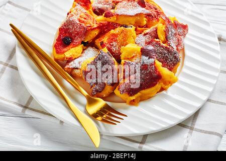 Dessert autrichien, crêpe douce et râpée kaiserschmarrn avec raisins secs et sucre glace sur le dessus servi sur une plaque blanche avec des couverts dorés sur une languette en bois Banque D'Images