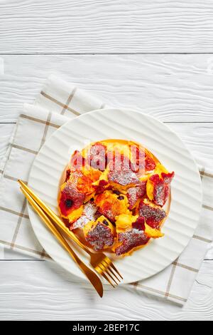 Crêpe sucrée autrichienne kaiserschmarrn avec raisins secs et sucre glace sur le dessus servi sur une plaque blanche avec des couverts dorés sur un backgrou en bois Banque D'Images