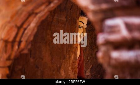 Vue sur une statue bouddhiste dans des tons rouges par une porte d'arche à Bagan, au Myanmar