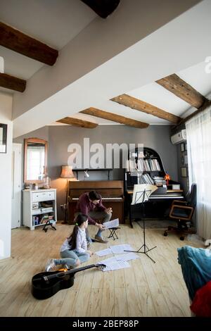 Jolie petite fille jouant de la guitare avec son professeur de musique dans l'appartement rustique Banque D'Images