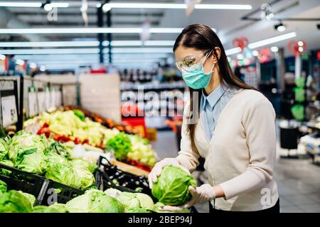 Femme avec masque hygiénique achetant dans un supermarché épicerie pour les verts frais, budget shopping pour les fournitures pendant la pandémie.Achat biologique végétabl Banque D'Images