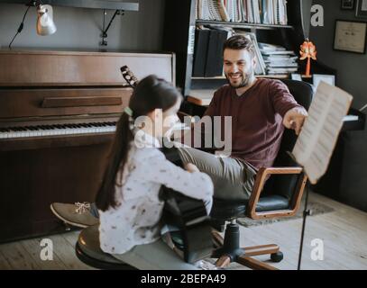 Jolie petite fille jouant de la guitare avec son professeur de musique dans l'appartement rustique Banque D'Images