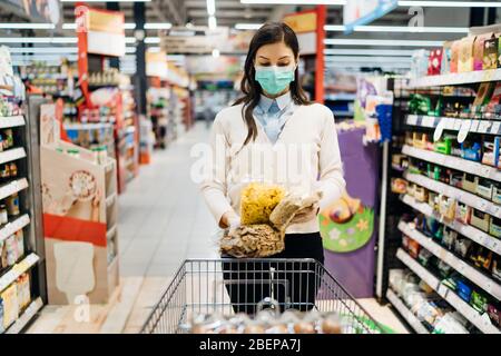 Femme avec masque faire des courses en toute sécurité au milieu de la pandémie de coronavirus dans une épicerie.COVID-19 achat de nourriture dans un supermarché.Panic buyin Banque D'Images