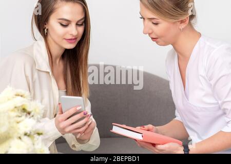 Le cosmologiste parle avec une jeune femme portant un peignoir regardant sur le smartphone du client. Banque D'Images