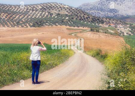 Femme photographiant le paysage avec une piste de campagne sinueuse près de Casabermeja, province de Malaga, Andalousie, sud de l'Espagne. Banque D'Images