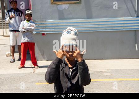 Un garçon de rue fait des panneaux de gang et semble menaçant. Il est avec ses amis. Les gangs sont populaires dans la communauté en Afrique du Sud. Banque D'Images