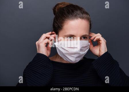 Leipzig. 31 mars 2020. Photo symbolique sur le sujet de la pandémie de corona, Covid-19 - UNE femme met sur un masque d'hygiène et se tient sur un fond gris, prise le 31 mars 2020 à Leipzig. A créé une photo symbolique. | utilisation dans le monde crédit: dpa/Alay Live News Banque D'Images