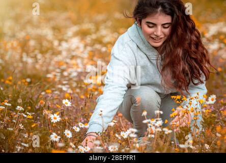 Adolescent profitant de vacances printanières dans la campagne, bonne fille heureuse avec plaisir choisir de petites fleurs de Marguerite, passer un temps de qualité à l'extérieur Banque D'Images