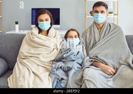 Famille malade dans les masques médicaux avec un plat assis sur un canapé regardant l'appareil photo avec de la fièvre à la maison attendant un médecin. Banque D'Images