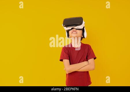 Jeune enfant portant des lunettes VR et surpris par une véritable animation sur fond jaune en studio Banque D'Images