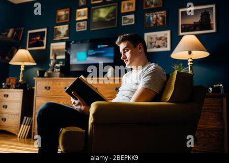 Homme appréciant la lecture d'un livre intéressant, maison seule en quarantaine.soins de santé mentale auto-soins, détente à la maison activité.Fun étudier, motivation d'éducation.Rouge Banque D'Images