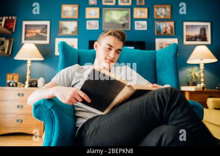 Homme appréciant la lecture d'un livre intéressant, maison seule en quarantaine.soins de santé mentale auto-soins, détente à la maison activité.étudier,apprendre,éducation.réduire Banque D'Images