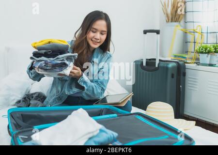 Préparation et planification de voyage sur le concept de vacances, Thaïlande et Asie heureuse femme emballage des vêtements dans le sac de valise à bagages pour voyager sur le lit Banque D'Images