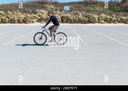 Un homme qui monte un vélo à travers un parking vide et déserté à Fistral à Newquay, en Cornwall. Banque D'Images