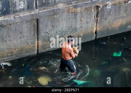 (200415) -- MANILLE, le 15 avril 2020 (Xinhua) -- un résident marche le long d'une rivière comme il porte son chien d'animal de compagnie qu'il a sauvé de sa maison brûlante dans une zone de taudis à Manille, aux Philippines, le 15 avril 2020. Plus d'une centaine de familles ont été déplacées dans l'incendie, selon le bureau de gestion des catastrophes de Manille, mercredi. (Xinhua/Rouelle Umali) Banque D'Images