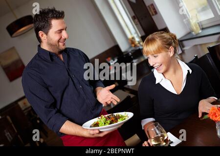 Le serveur apporte la salade à une femme au restaurant Banque D'Images